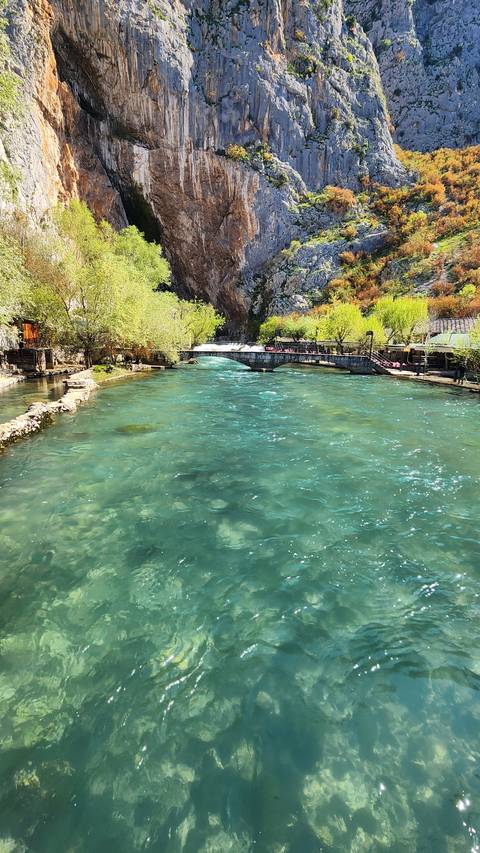 Clear blue river with rocky cliffs and greenery.