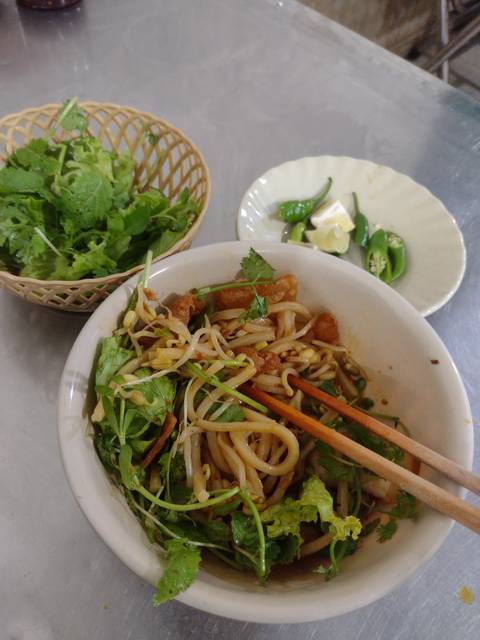       A bowl of noodles with vegetables and herbs.
  