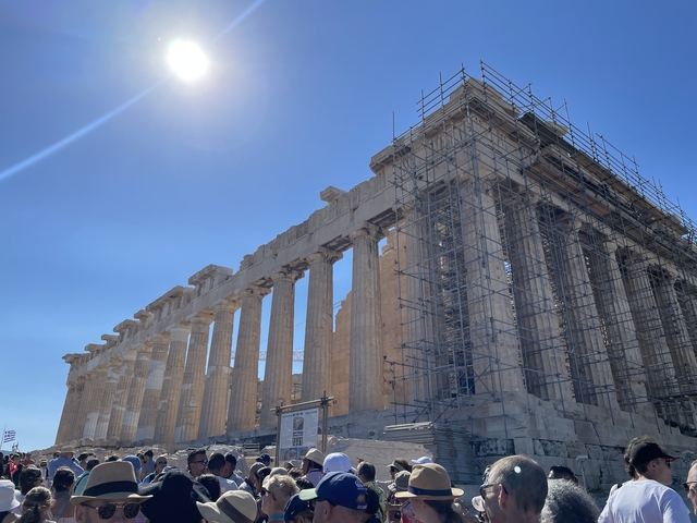       View of the Parthenon under restoration work, against a bright blue sky.
  