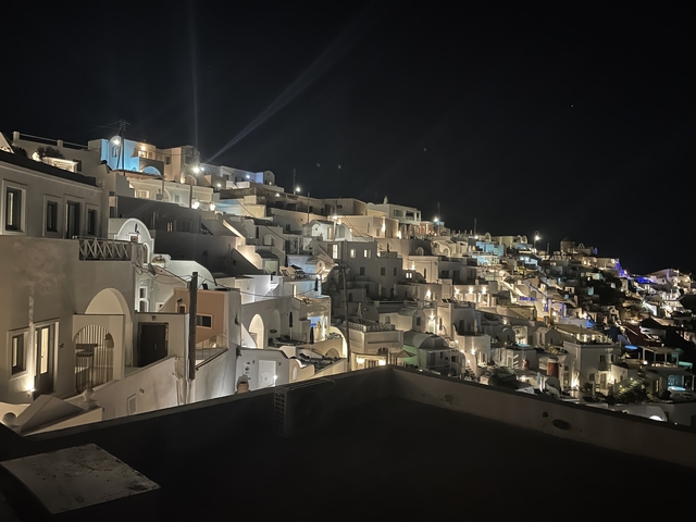       Illuminated hillside town at night with traditional white architecture.
  