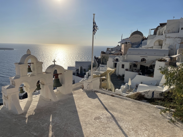       Sunset view over the sea with iconic Santorini architecture, featuring a church bell tower.
  
