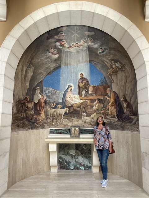 Woman standing in front of a large mural depicting the Nativity scene.
