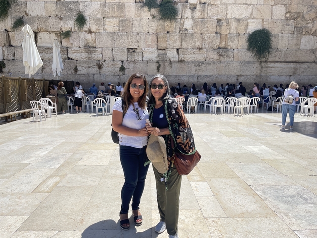 Two women smiling in front of the Western Wall in Jerusalem.