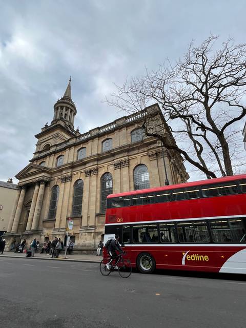       Red double-decker bus passing by a historic building.
  