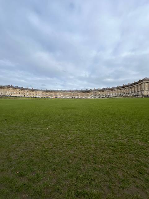       Panoramic view of a grassy field with historic buildings in the background.
  