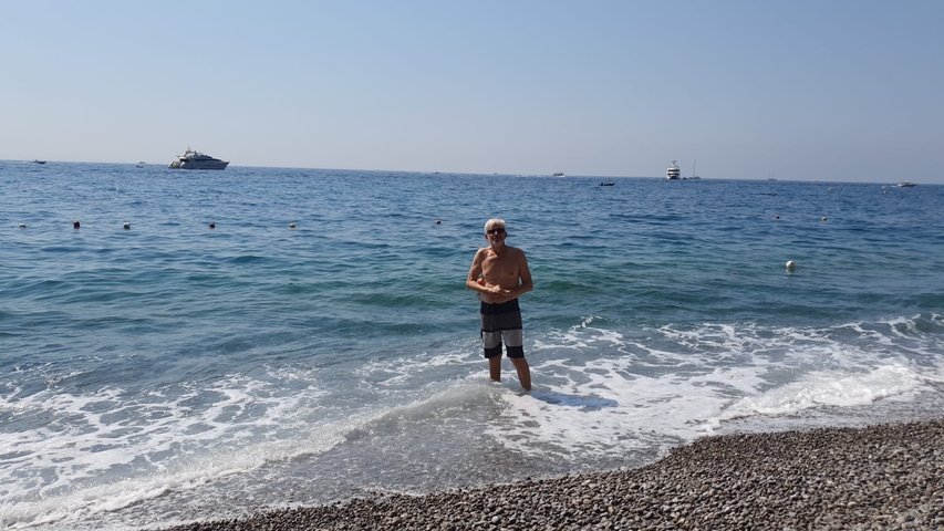       Man standing in the sea with boats in the distance
  