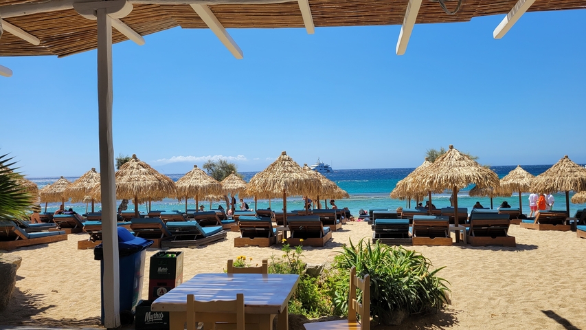 Beach scene with straw umbrellas and loungers overlooking the sea.