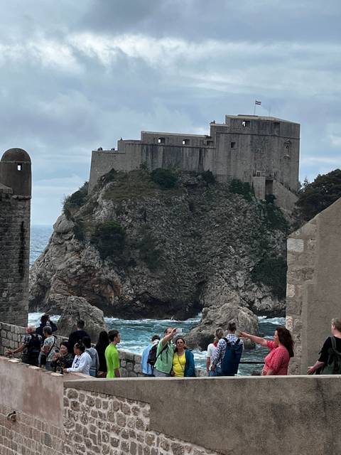       View of a medieval stone fortress with people exploring.
  