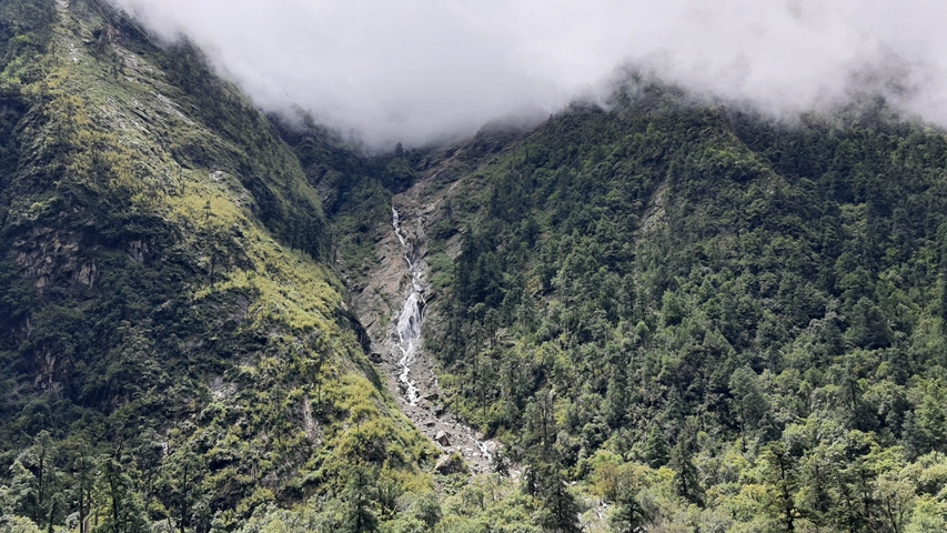 A scenic view of a mist-covered waterfall in a lush mountain landscape.