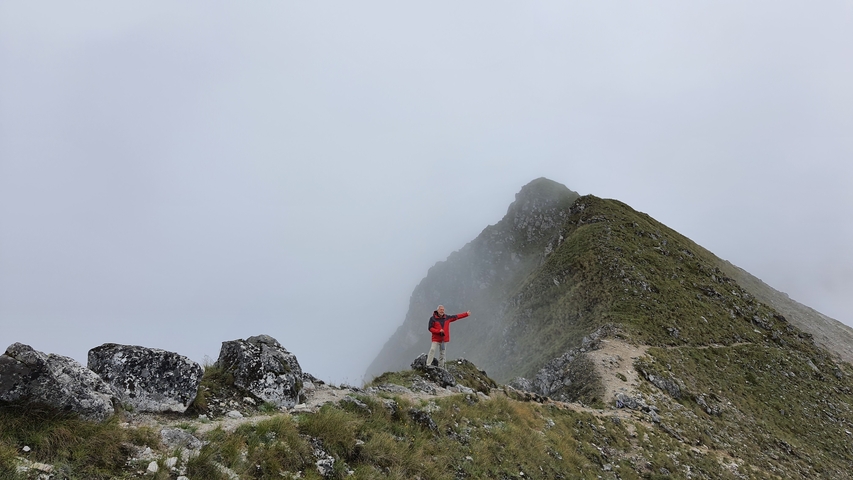 A person in a red jacket standing on a misty ridge trail.