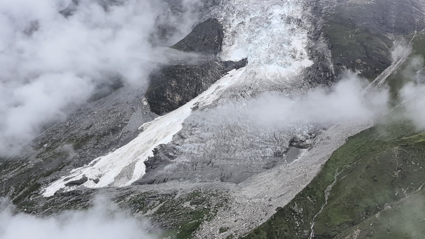 A glacier descending a rock face, partially covered by clouds.