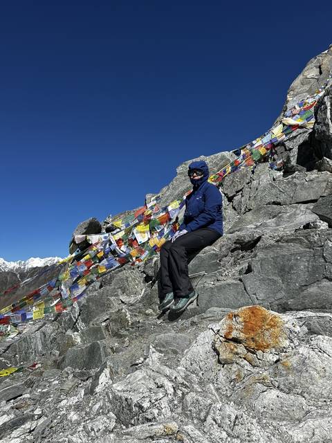 Person climbing rocky landscape with prayer flags