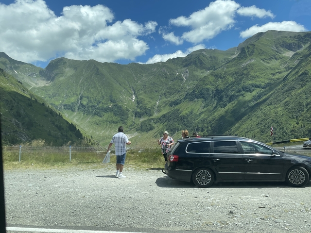 A group of people by a car overlooking mountains.