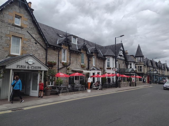 A bustling street scene outside a traditional English Fish & Chips shop.