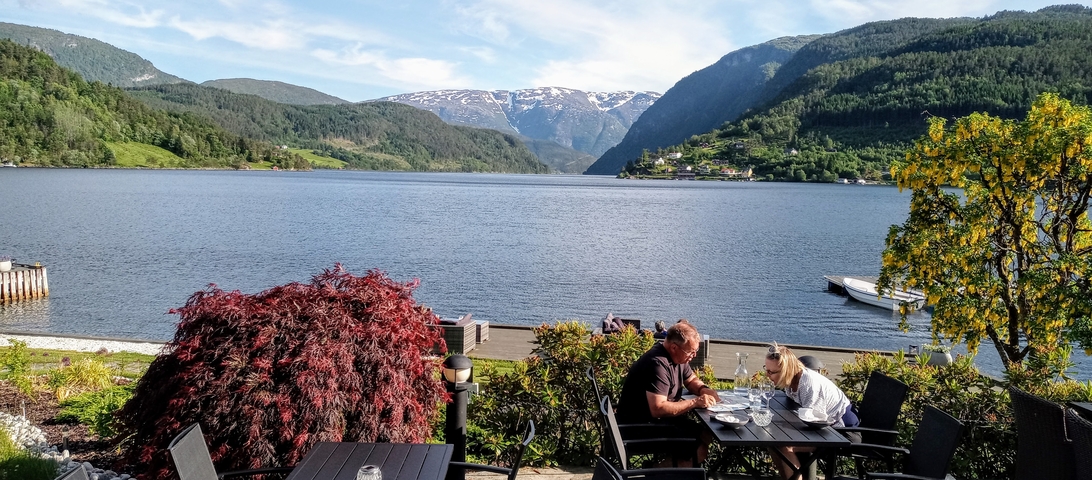       A couple dining by the water with mountain views.
  