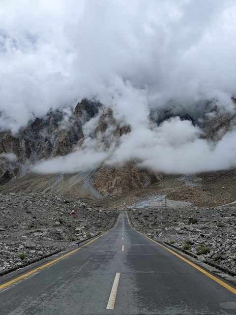       Fog-shrouded mountains with a rocky road in the foreground.
  