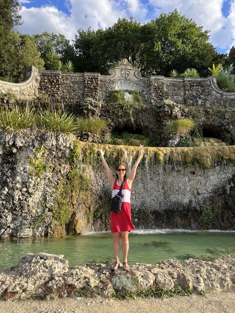       Woman with raised arms in front of a rocky waterfall.
  