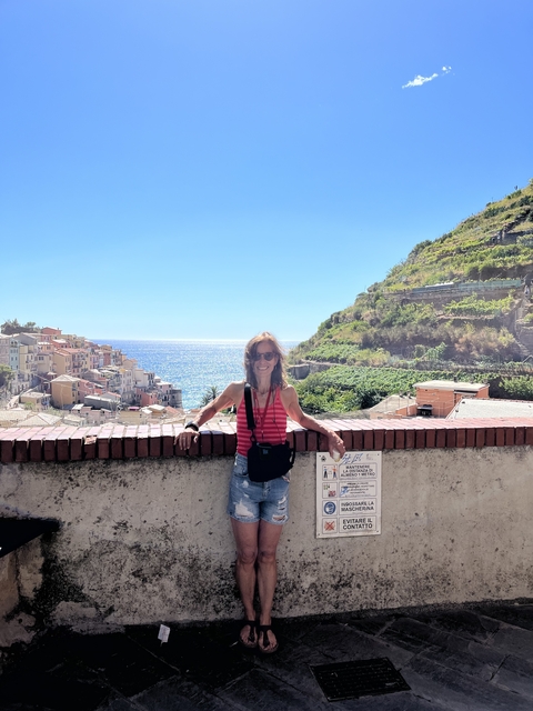       Woman posing on a terrace overlooking the sea and terraced buildings.
  
