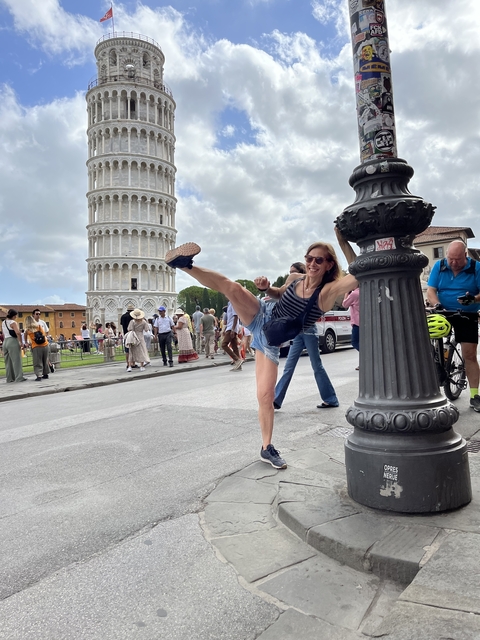       Woman playfully posing for a photo in front of the Leaning Tower of Pisa.
  