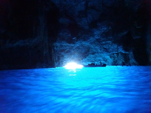       Inside a dark cave with blue illuminated waters.
  