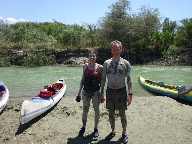       Two people covered in mud standing beside canoes.
  