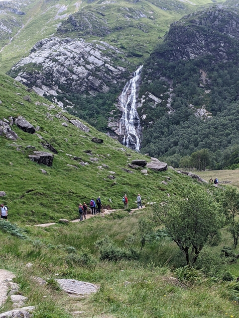 Hikers walking on a trail towards a waterfall.