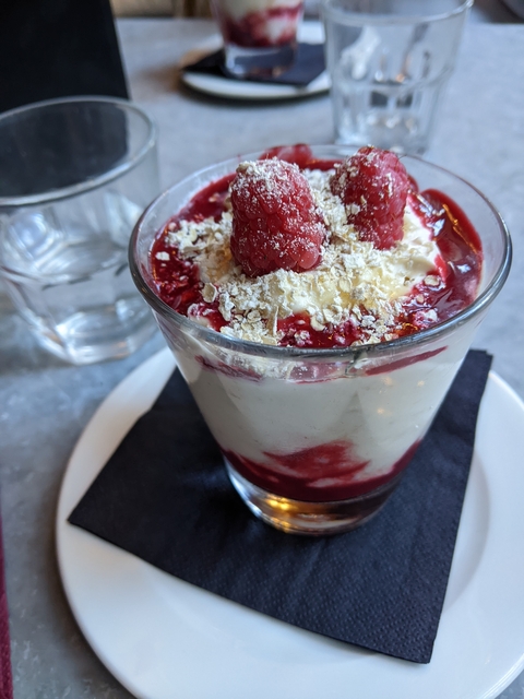 Dessert in a glass with raspberries and cream.