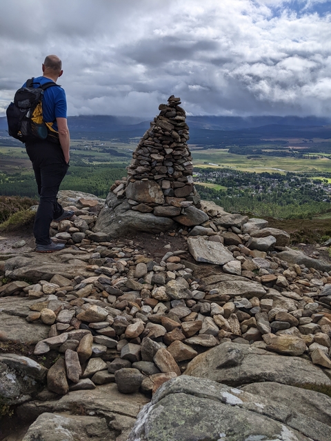 Man standing by a cairn on a mountain top.