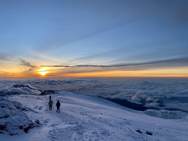 Snowy mountain landscape with two people walking at sunrise.