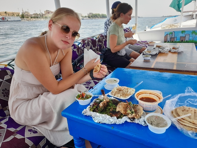       People dining on a boat with food and river view.
  