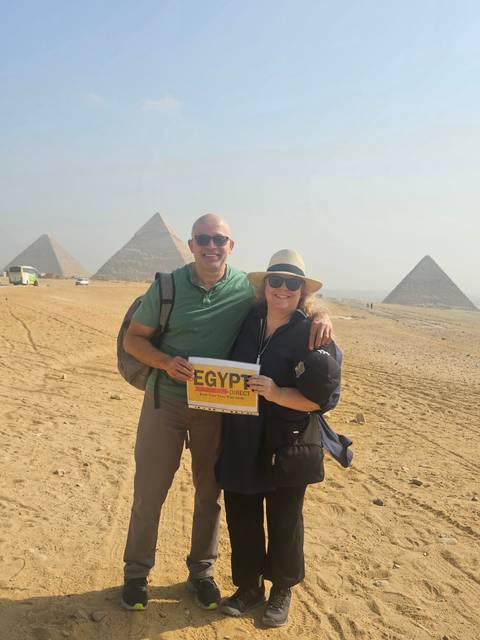       Two people posing with the pyramids in the background, holding a sign.
  