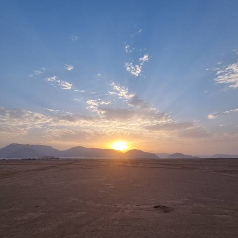 Sunset over a desert landscape with distant mountains.