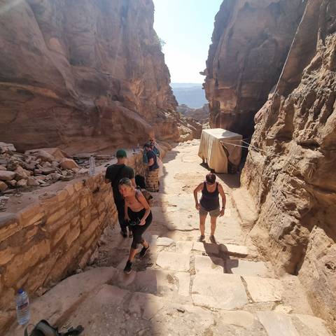       People walking on a rocky path with tents and mountains in the background.
  
