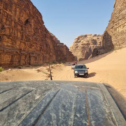 Off-road vehicle driving through a canyon with rocks and sand.