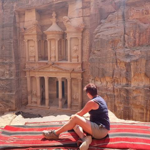       Person sitting on a carpeted area overlooking an ancient stone facade.
  