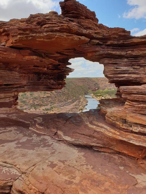       A scenic view through a natural rock arch with landscape in the background.
  