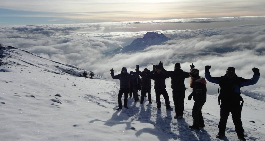 Group of hikers on a snowy mountain with stunning cloud views.