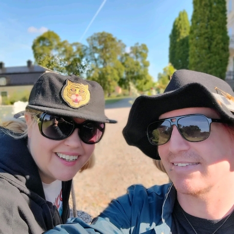       Two people smiling and wearing hats outdoors.
  