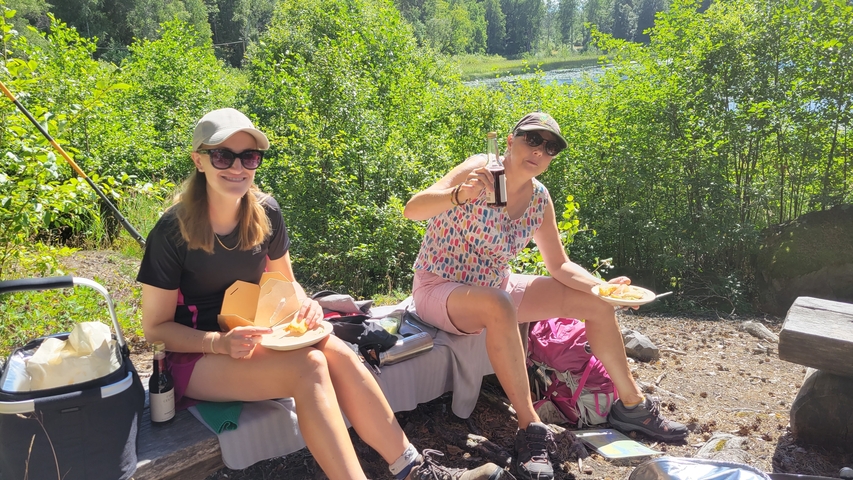 Two women enjoying a meal outdoors with a lake view.
