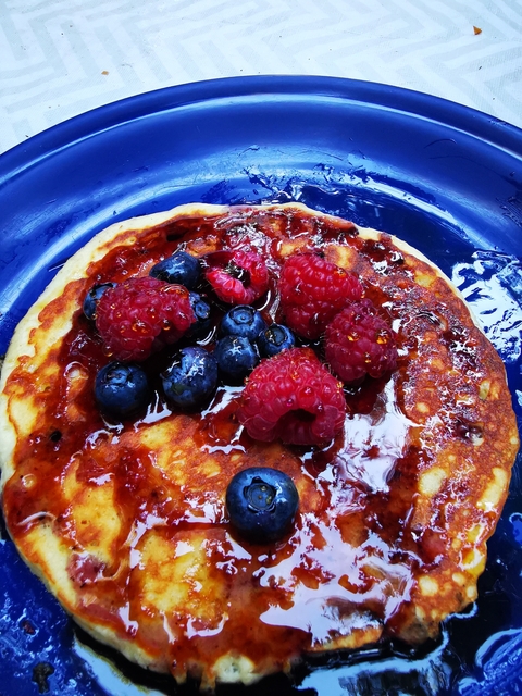 A pancake with raspberries and blueberries on a blue plate.