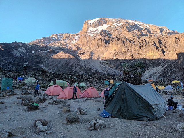 A campsite with colorful tents set below a massive rocky mountain.