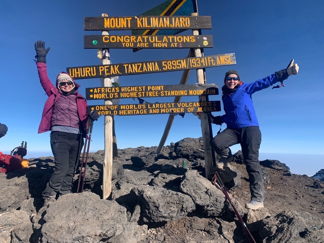 Two people posing at Uhuru Peak with a sign.