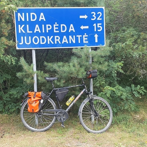       A bicycle parked by a sign pointing to Juodkrante.
  