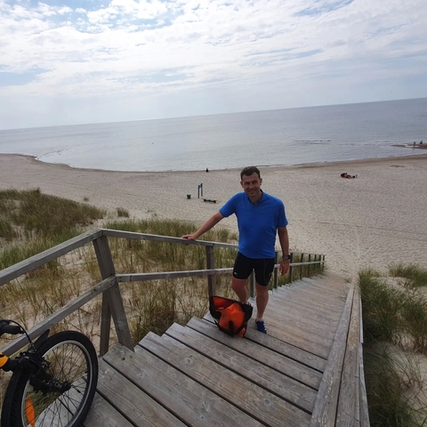 A man in a blue shirt standing on steps leading to the beach.