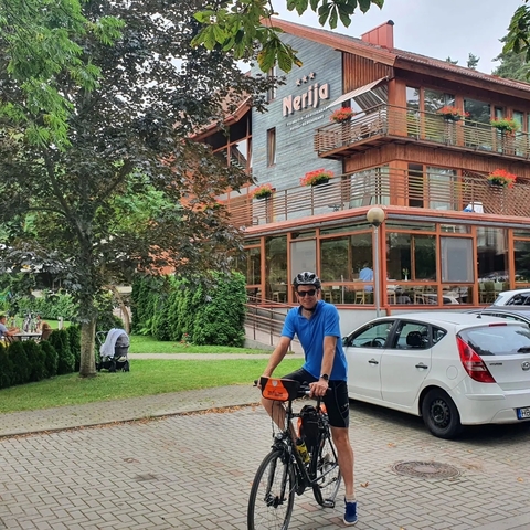 A man in a blue shirt cycling near a wooden building.