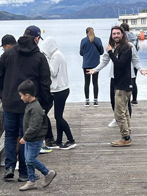       People standing on a wooden jetty at a lake.
  