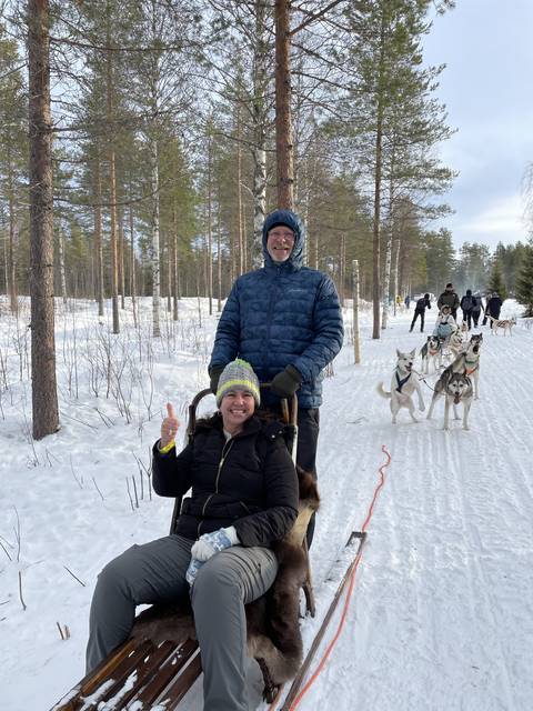 Couple on a dog sled ride in a snowy forest.