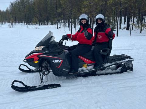 Two people with snowmobile in snowy landscape.