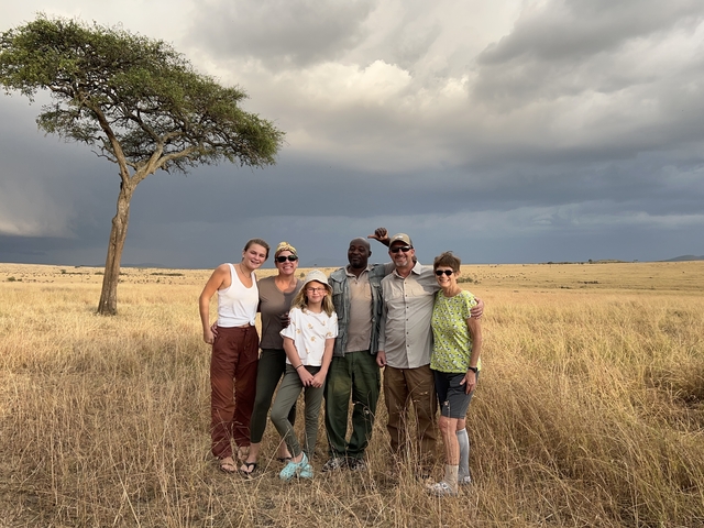 Group of people posing on a savanna with a tree under a cloudy sky.