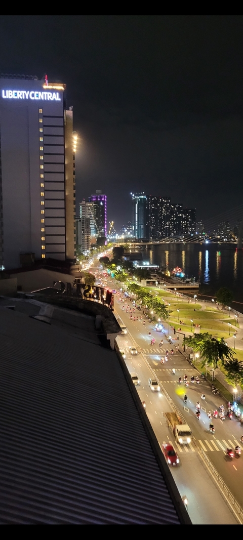 A night view of a lit street next to a river with distant buildings.